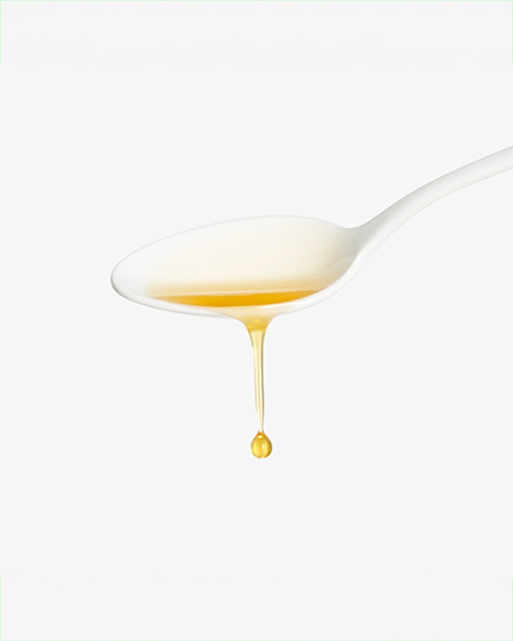 A close-up of a white spoon holding golden liquid collagen, with a single drop dripping from the bottom against a white background.
