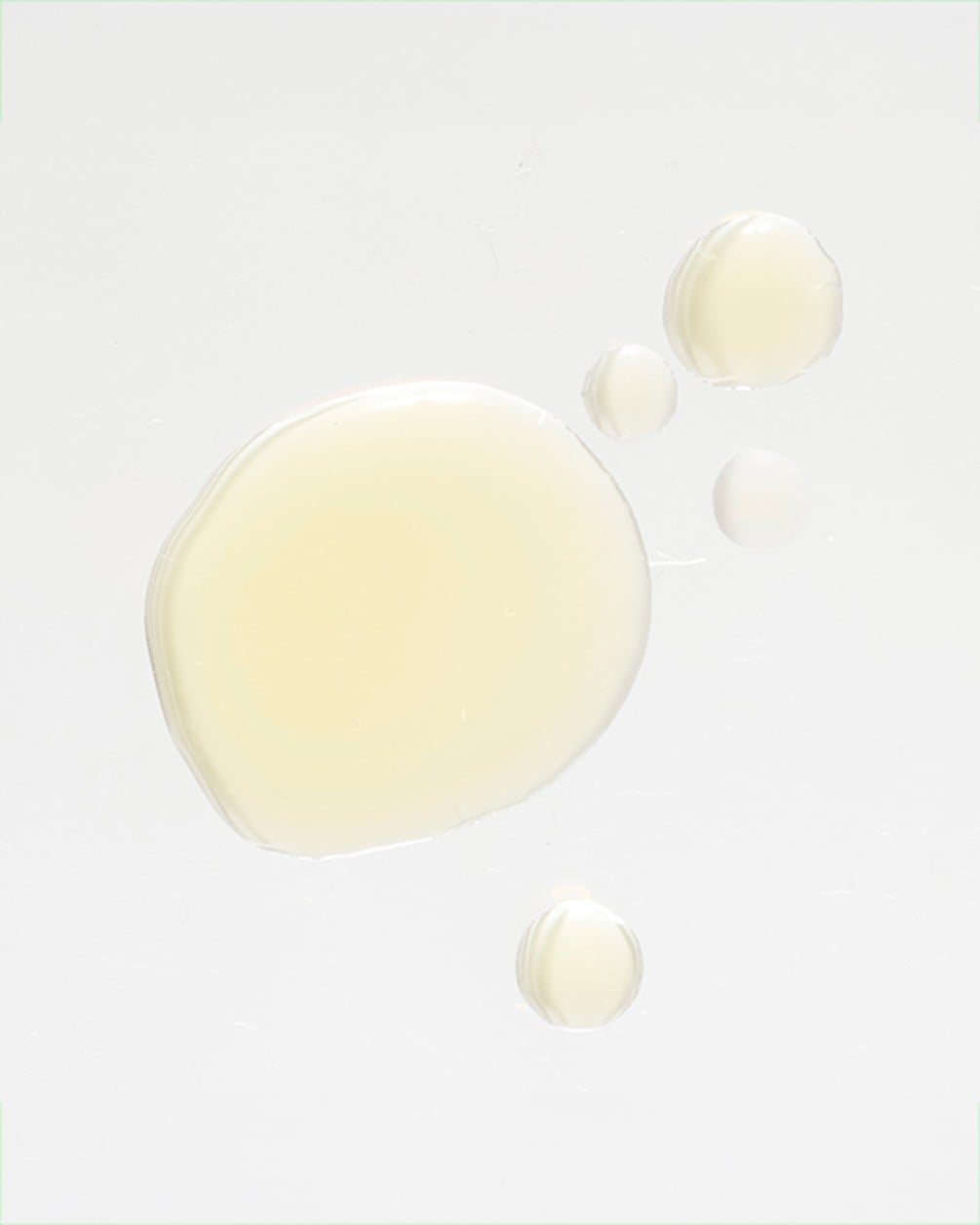 A top-down view of several golden, translucent droplets of liquid collagen scattered on a clean white surface.