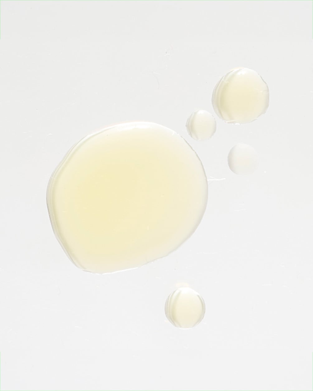 A top-down view of several golden, translucent droplets of liquid collagen scattered on a clean white surface.