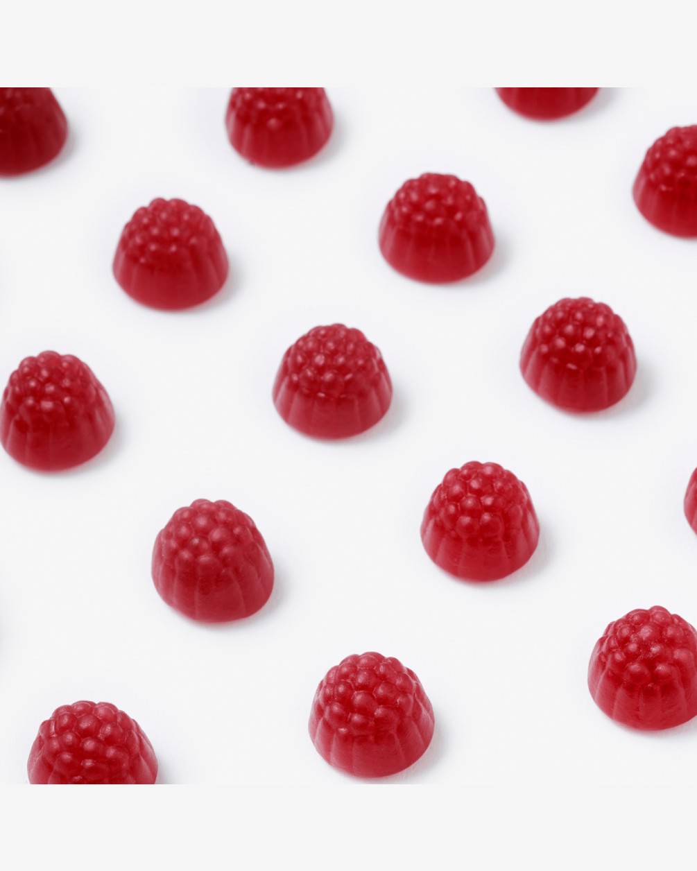 Multiple red, raspberry-shaped gummy L30 supplements are arranged in neat, diagonal rows on a clean white surface.