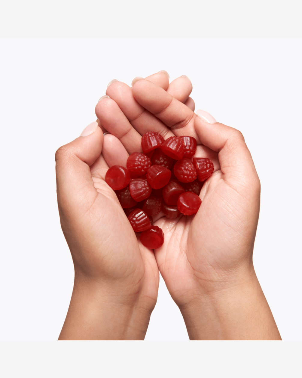 Two hands cupped together, holding a large pile of red, raspberry-shaped gummy L30 supplements against a plain white background.