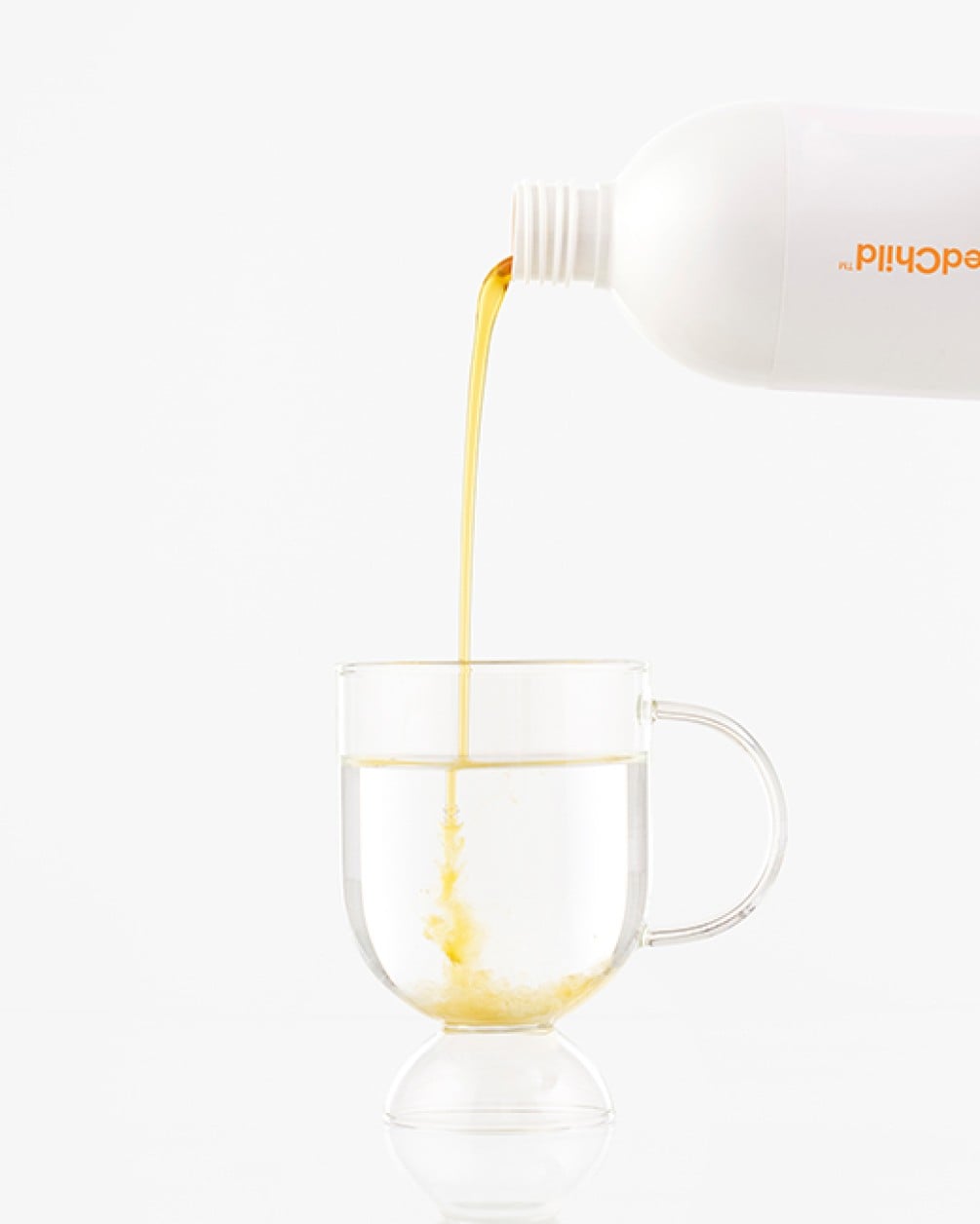 A white bottle pouring golden mango liquid collagen into a clear glass mug of water against a white background.