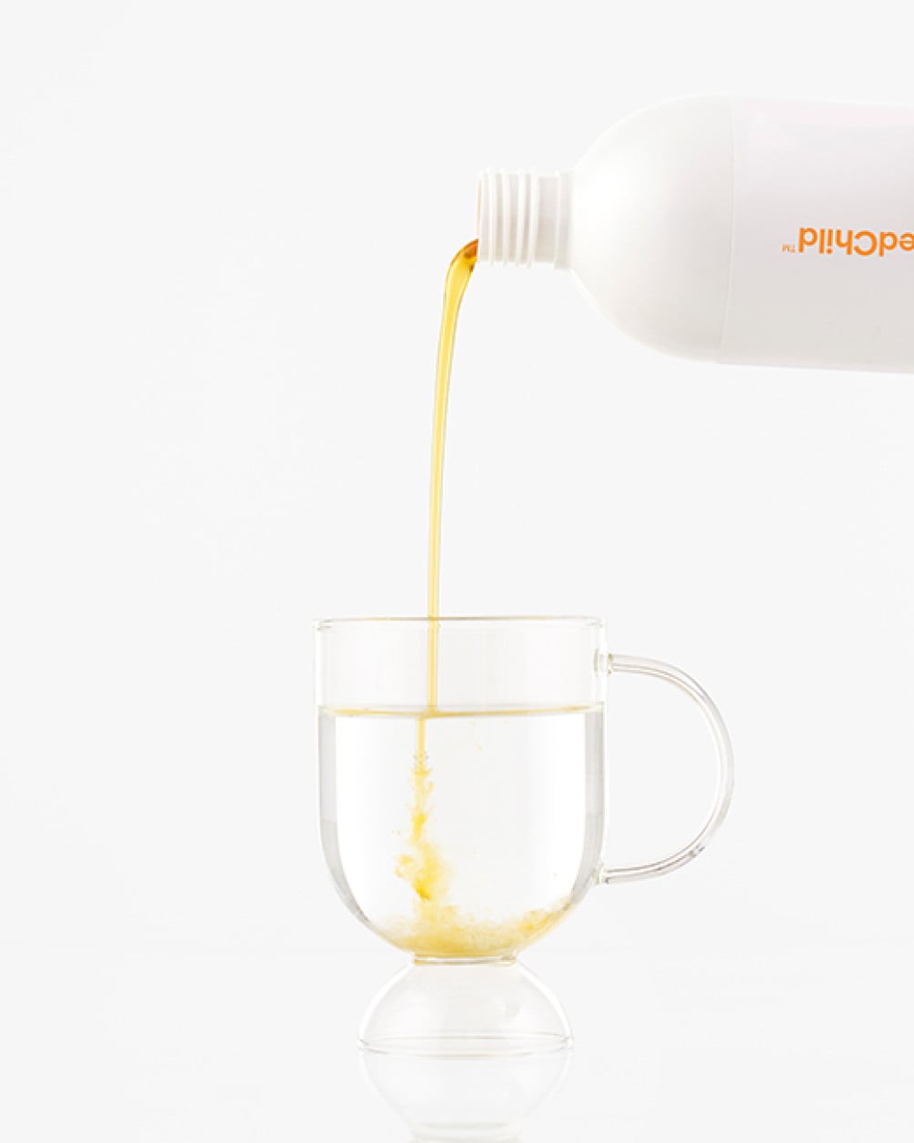 A white bottle pouring golden mango liquid collagen into a clear glass mug of water against a white background.