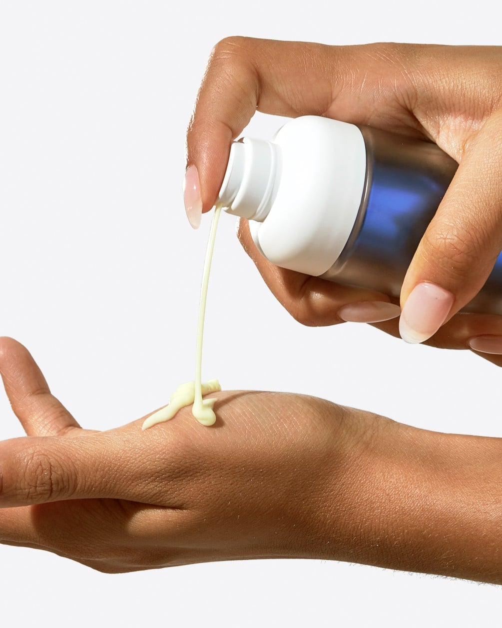 A close-up action shot of a person with a medium-to-deep skin tone dispensing a white, creamy serum from a SpoiledChild F38 bottle with a blue metallic label onto the back of their hand.