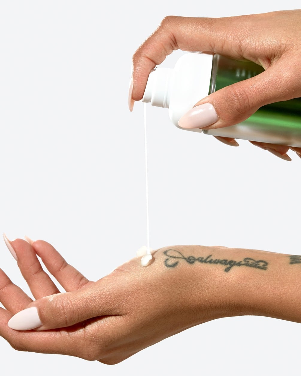 Primer plano de una persona de tono de piel medio a oscuro aplicando un sérum blanco y cremoso desde una botella A35 de SpoiledChild, con etiqueta verde metálico, sobre el dorso de su mano.