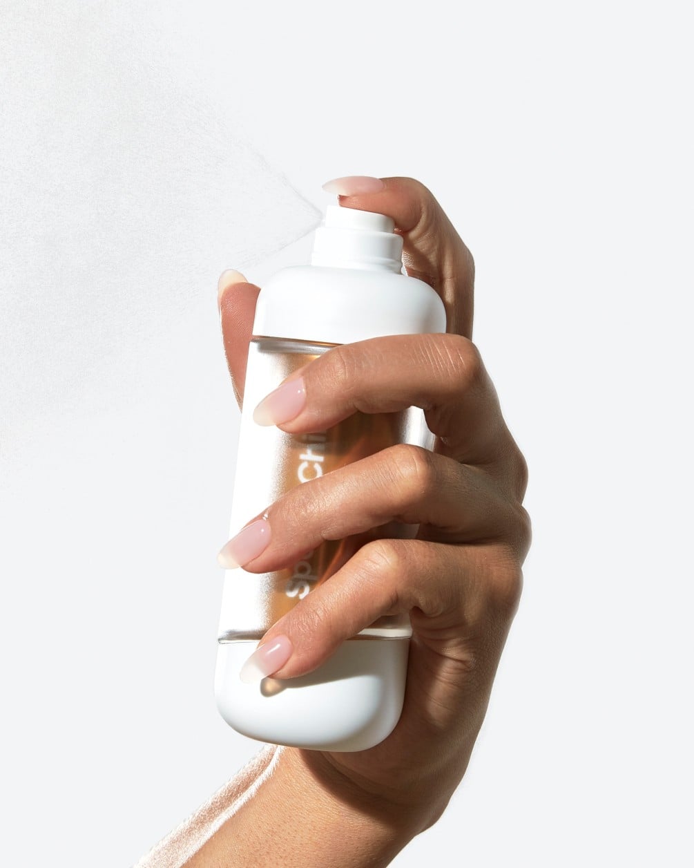 A hand with manicured nails holds a white SpoiledChild A22 spray bottle and presses the nozzle, releasing a fine mist.
