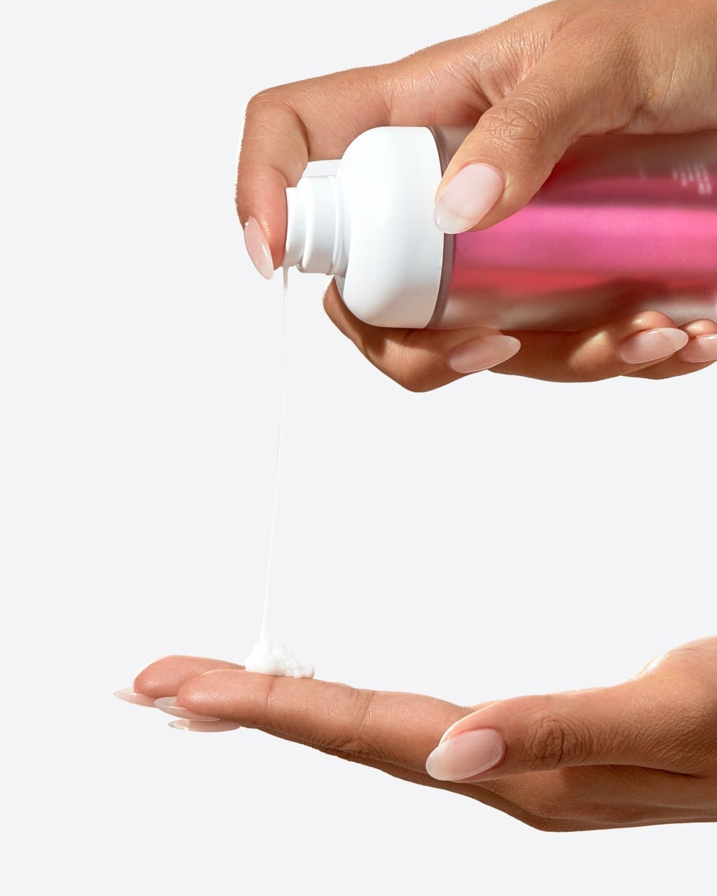 A close-up action shot showing a person with a deeper skin tone dispensing a creamy liquid from a white SpoiledChild O36 pump bottle. A small amount of the product is shown landing in the palm of their other hand.