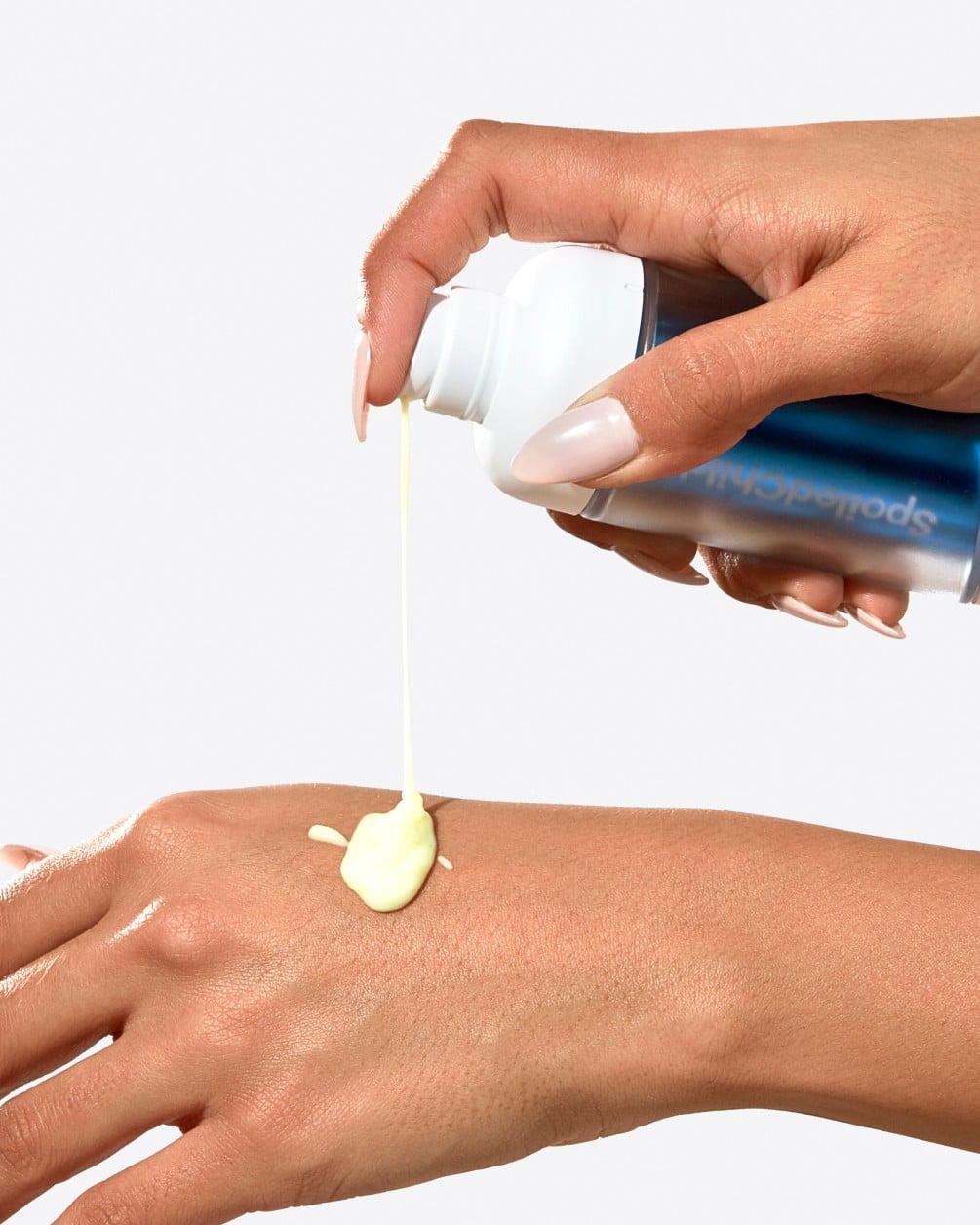 An action shot showing a hand dispensing a creamy, light-yellow product onto the back of another hand. The product is being squeezed from a white G25 bottle with a blue metallic label, illustrating the texture and application of the serum.
