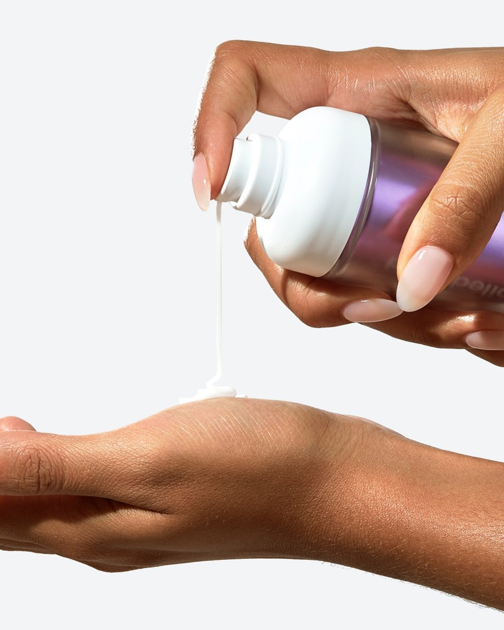 A close-up action shot showing a person with a deeper skin tone dispensing a creamy liquid from a white SpoiledChild C29 pump bottle. A small amount of the product is shown landing in the palm of their other hand.