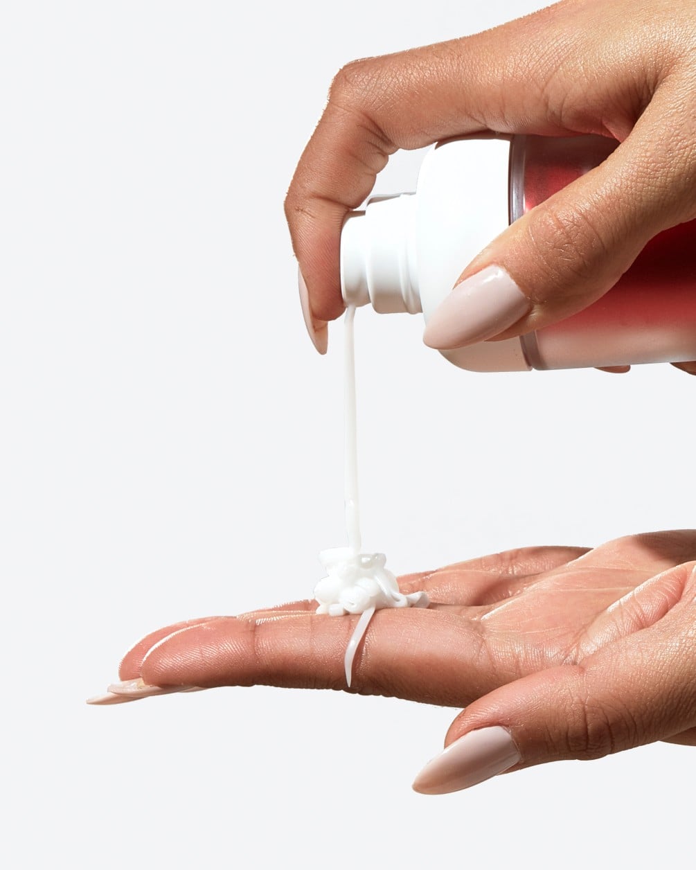 A close-up action shot showing a person with a deeper skin tone dispensing a creamy liquid from a white SpoiledChild D35+ pump bottle. A small amount of the product is shown landing in the palm of their other hand.