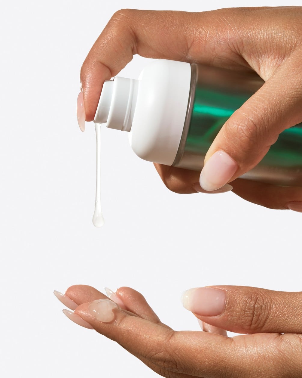 A close-up of a person with a neutral-toned manicure dispensing a clear, gel-like liquid from a white and teal SpoiledChild M27 pump bottle onto their open palm. The image is set against a clean, white background.