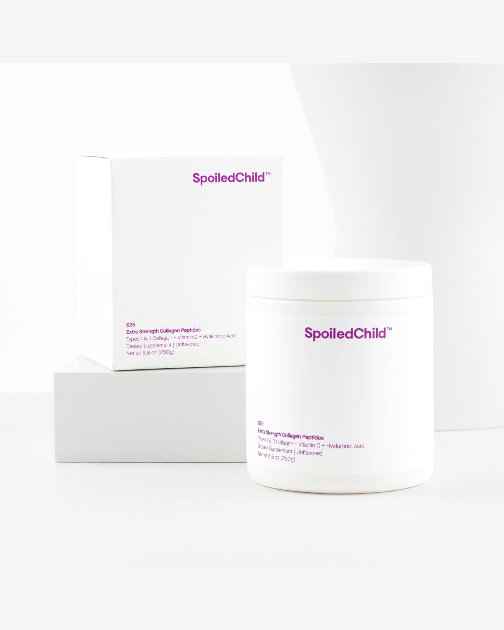 A white tub of SpoiledChild S25 Extra Strength Collagen Peptides stands in the foreground, with its corresponding white product box resting on a white block in the background. The scene is set against a clean, minimalist white backdrop.