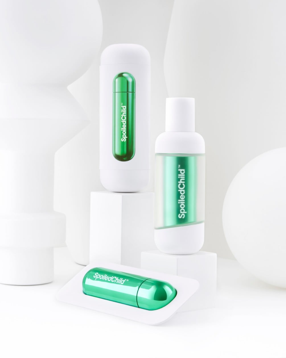 A minimalist product arrangement of SpoiledChild S34 skincare items on white geometric pedestals against a clean white background. The set includes two white bottles and a separate metallic green refill.