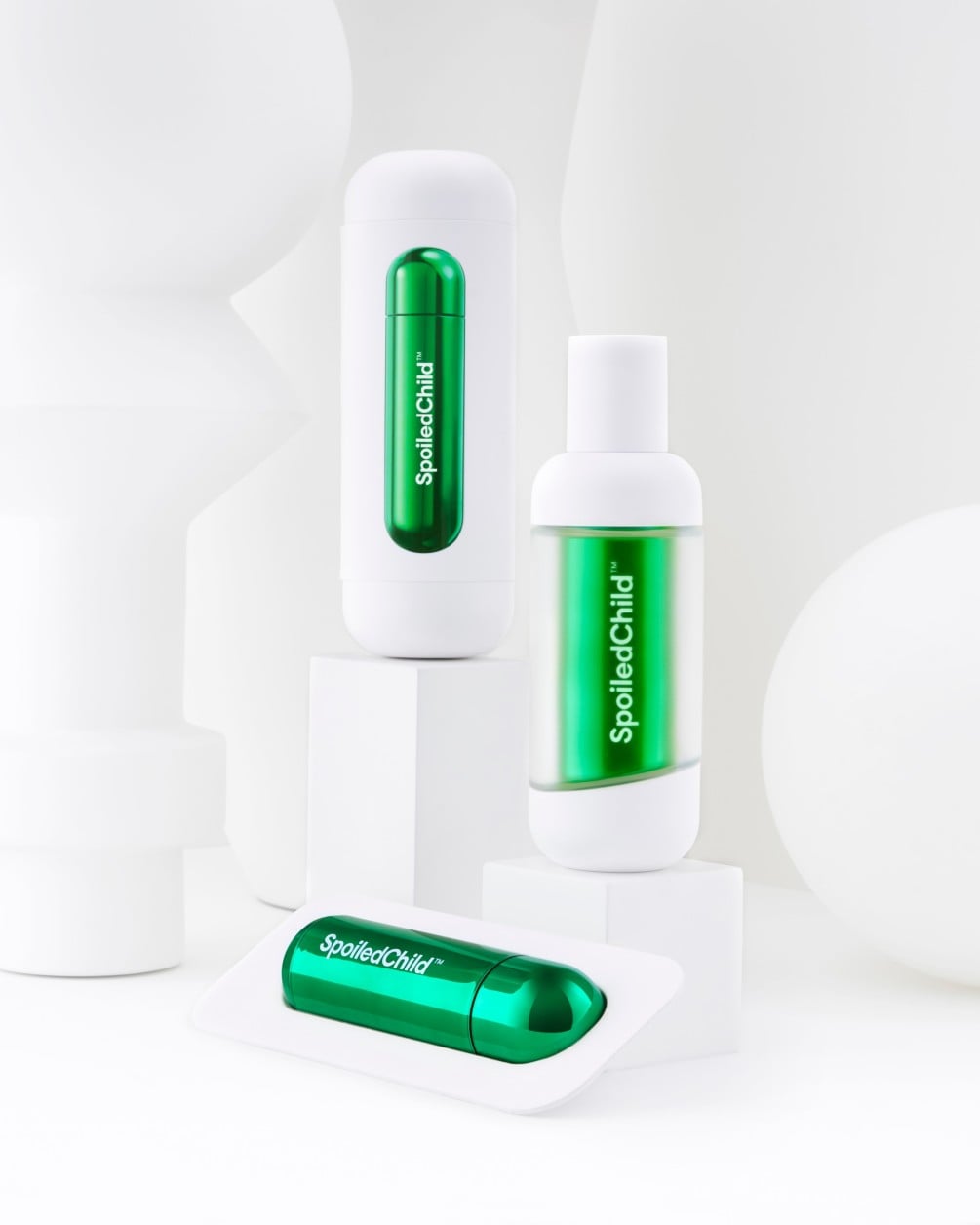 A product arrangement on white geometric pedestals featuring the M27. The display includes a tall white container with a green refill window, a smaller bottle with a clear body showing a metallic green capsule, and a single green refill capsule resting on