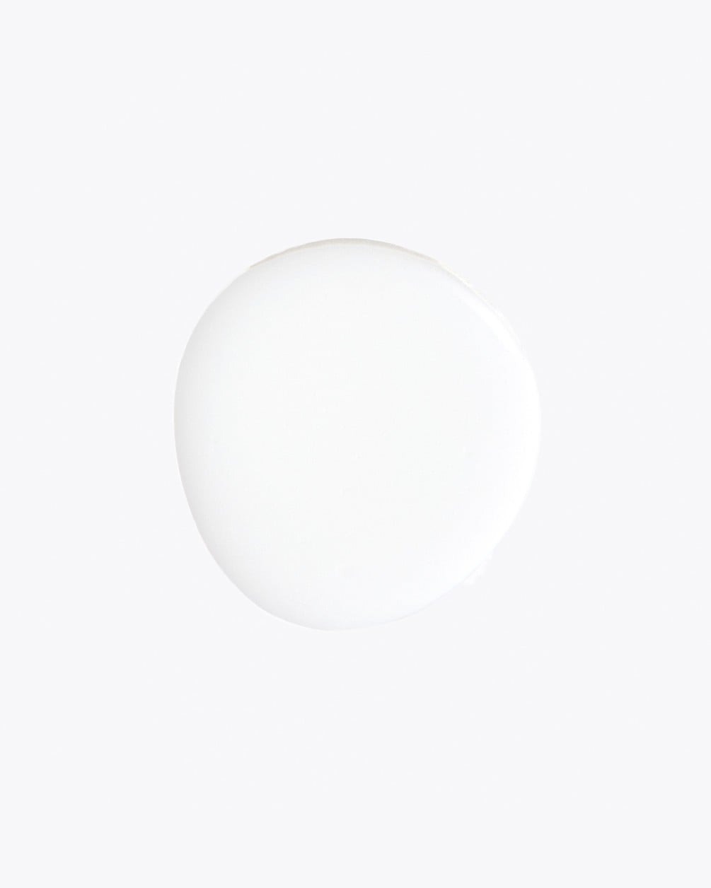 Plano cenital de una gota de líquido blanco de forma circular sobre un fondo blanco.