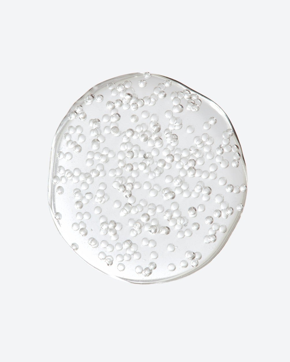 Overhead shot of a circular drop of clear, translucent gel filled with small white oxygenating bubbles on a white background.
