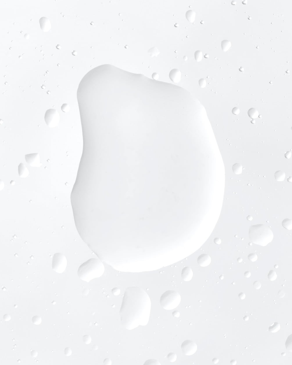 A close-up shot of a large, clear, liquid droplet surrounded by smaller droplets on a light gray surface.