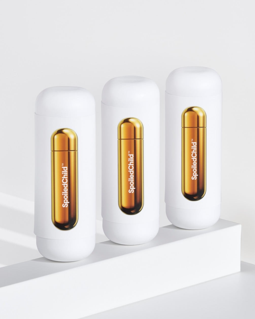 Three white SpoiledChild A22 bottles with metallic copper refill capsules displayed in a row on a white stepped surface.