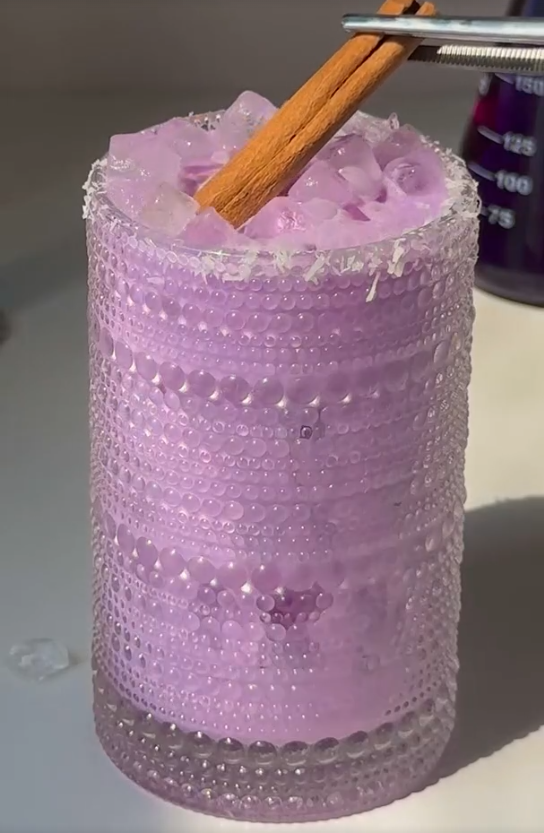 Glass of creamy purple ube collagen horchata over ice with a cinnamon stick and salted rim