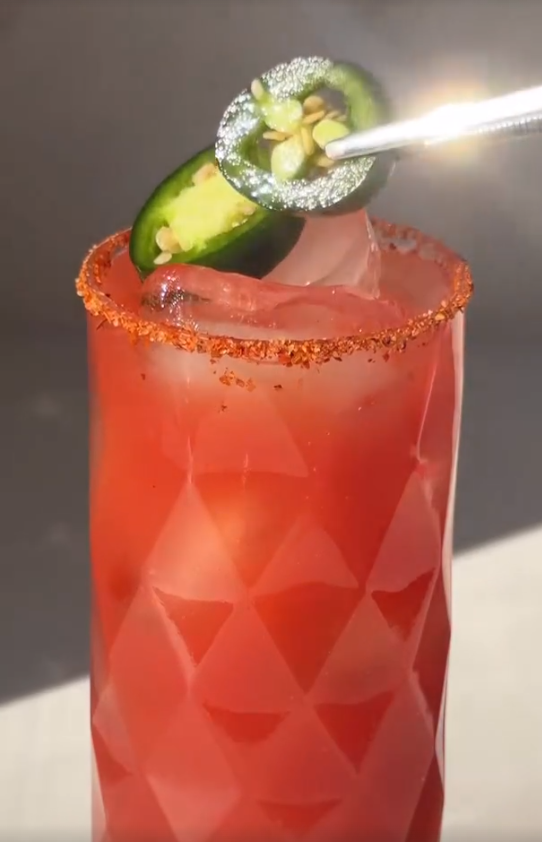 Tall glass of red guava collagen mocktail with a chili-salt rim and fresh jalapeño slices