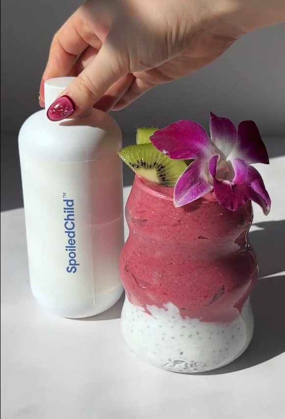 Layered tropical smoothie with a pink raspberry-pitaya top over a coconut-yogurt chia base, garnished with kiwi slices and an orchid, in a tall glass