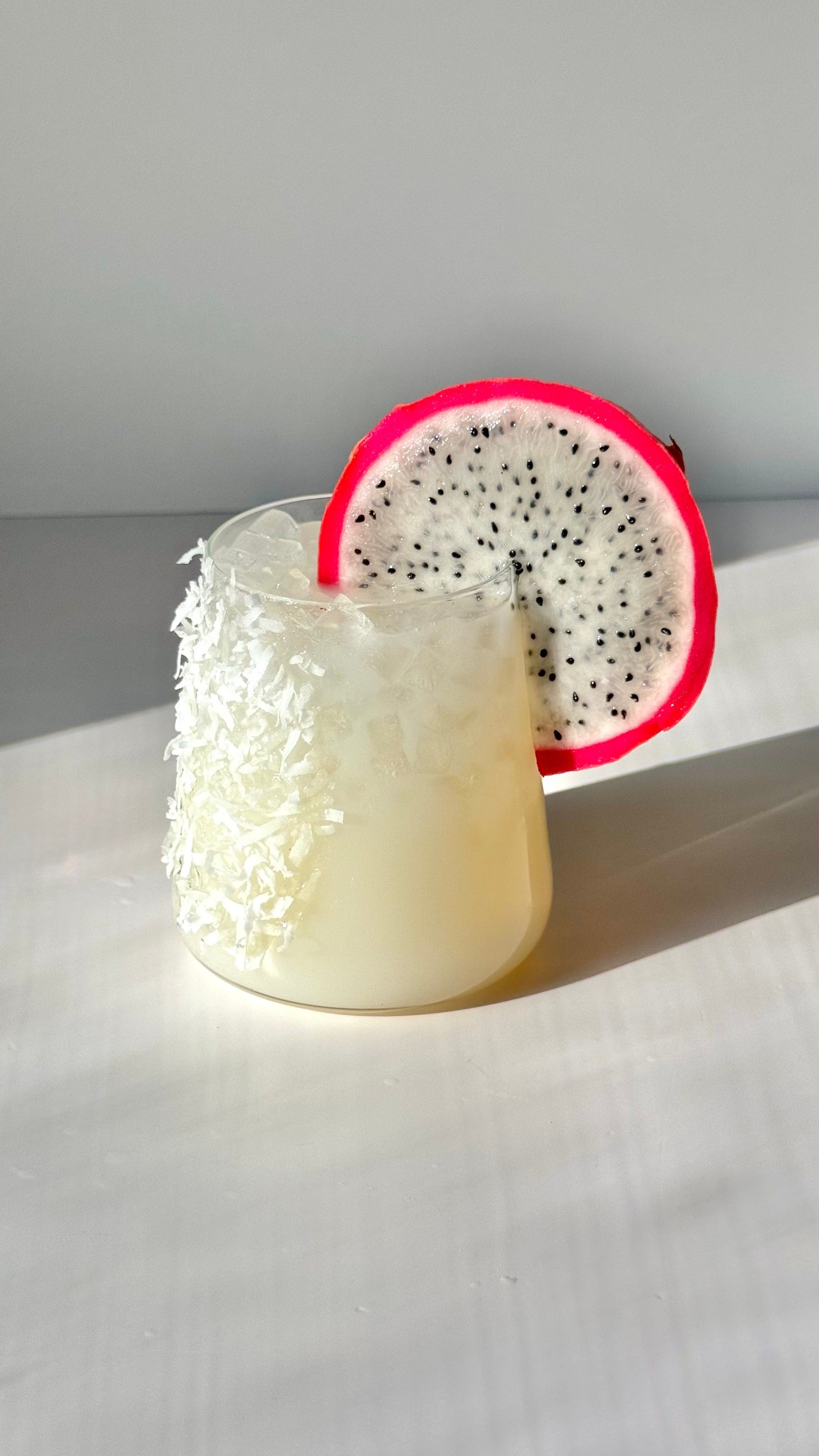 Creamy lychee collagen margarita mocktail with a coconut-flake rim and dragon-fruit slice, next to a SpoiledChild E27 bottle
