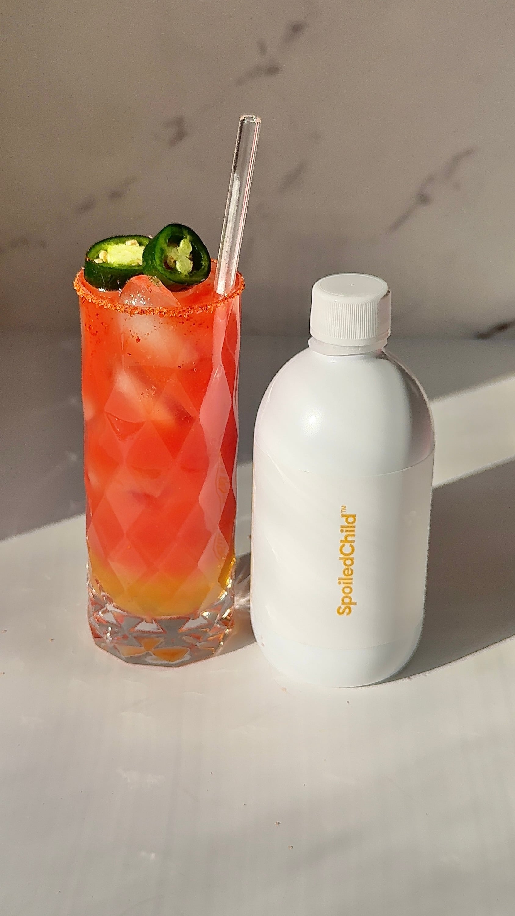 Tall glass of red guava collagen mocktail with a chili-salt rim and fresh jalapeño slices